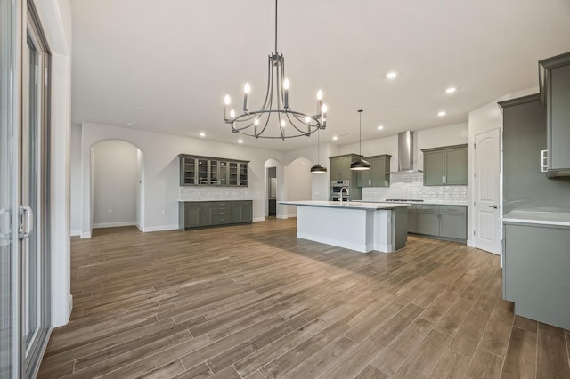 kitchen featuring pendant lighting, tasteful backsplash, gray cabinetry, a center island with sink, and wall chimney exhaust hood