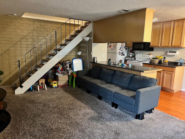 living area featuring a textured ceiling, brick wall, visible vents, light wood-style floors, and stairway