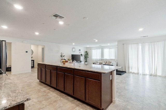 kitchen with light stone countertops, dark brown cabinets, and a center island with sink