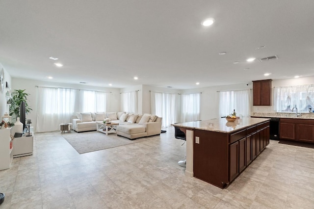 kitchen featuring sink, a kitchen breakfast bar, dark brown cabinetry, light stone countertops, and a kitchen island