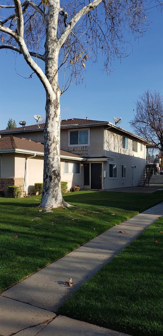 view of front facade featuring stairs, a front yard, and stucco siding