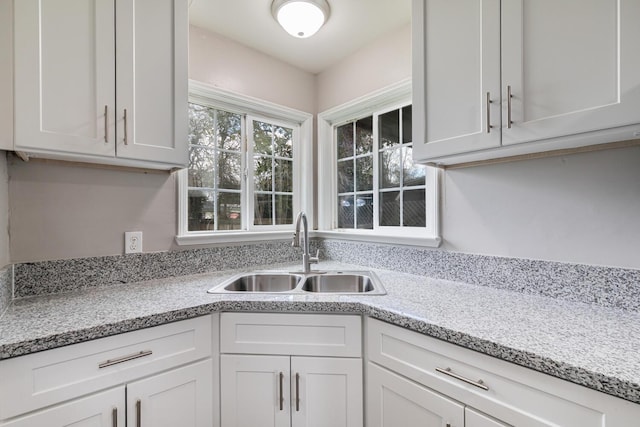 kitchen featuring light stone counters, sink, and white cabinets