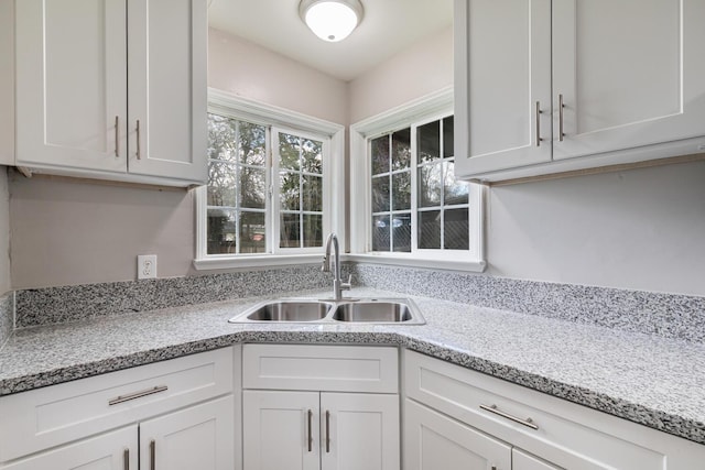 kitchen with white cabinets, light stone countertops, and a sink