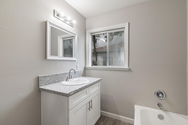 full bath featuring a bathing tub, wood finished floors, vanity, and baseboards