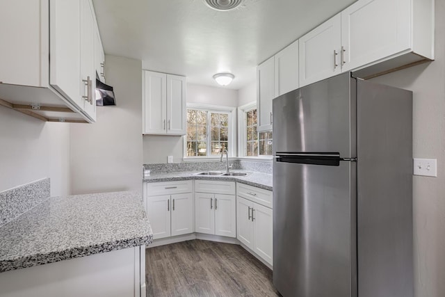 kitchen with light stone counters, white cabinetry, freestanding refrigerator, a sink, and wood finished floors