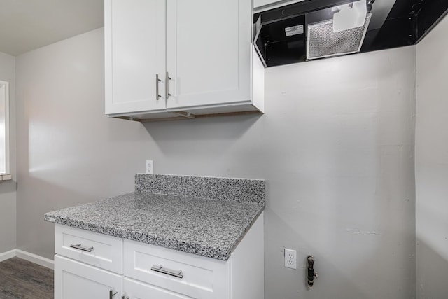 kitchen with baseboards, white cabinetry, light stone countertops, dark wood-type flooring, and range hood