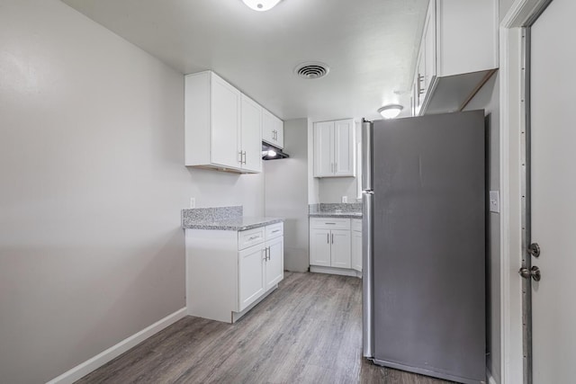 kitchen with white cabinets, light stone countertops, stainless steel fridge, and light hardwood / wood-style floors