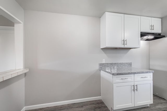 kitchen featuring dark wood-style flooring, baseboards, white cabinetry, and under cabinet range hood