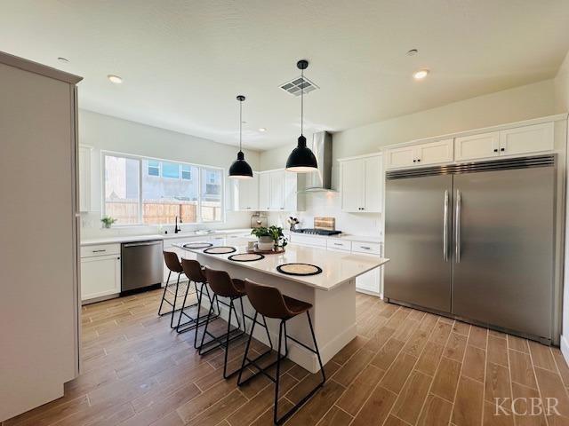 kitchen featuring light countertops, wall chimney range hood, light wood-style flooring, and appliances with stainless steel finishes