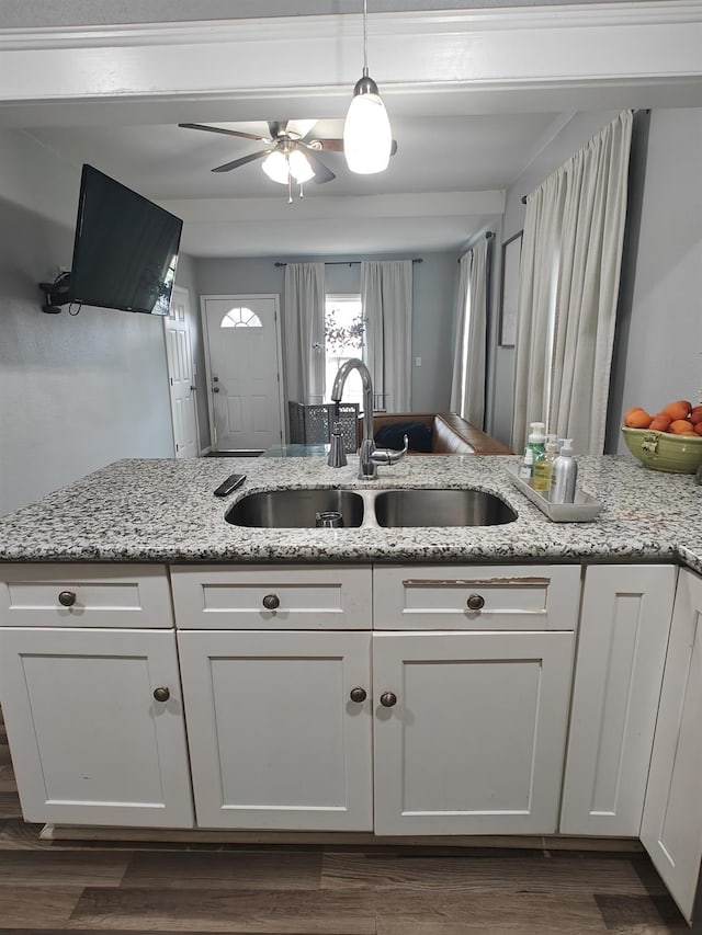 kitchen with light stone counters, white cabinetry, a sink, and decorative light fixtures