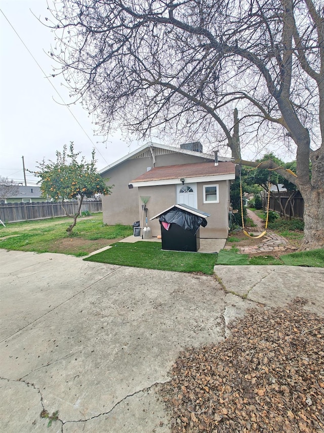 rear view of property featuring a lawn, fence, and stucco siding