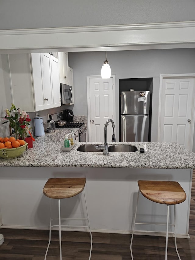 kitchen with stainless steel appliances, a peninsula, a sink, white cabinetry, and pendant lighting