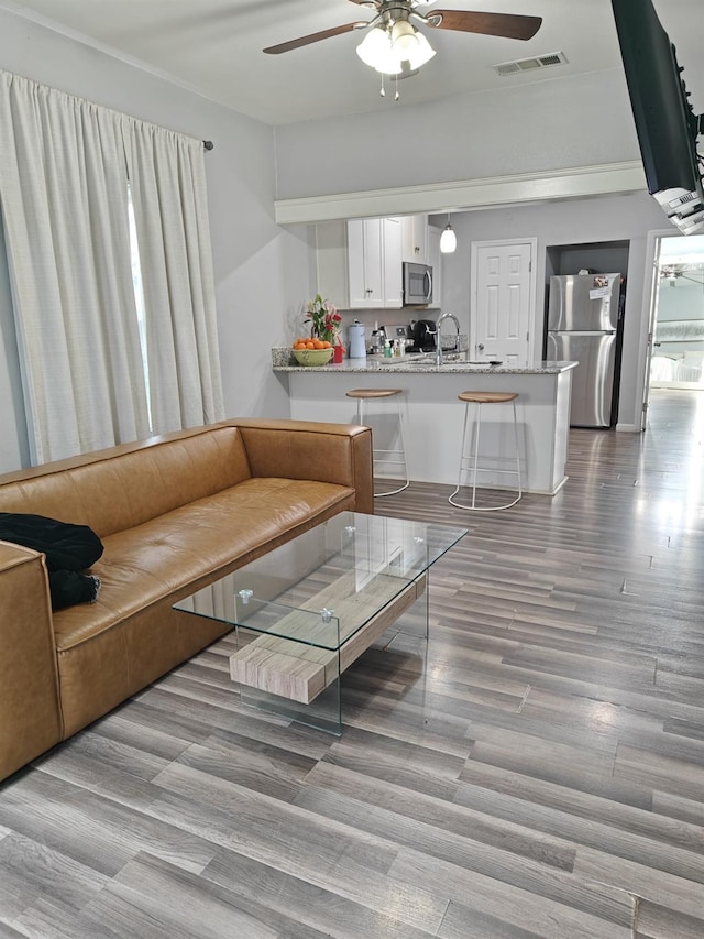 living room featuring light wood-style floors, visible vents, and ceiling fan