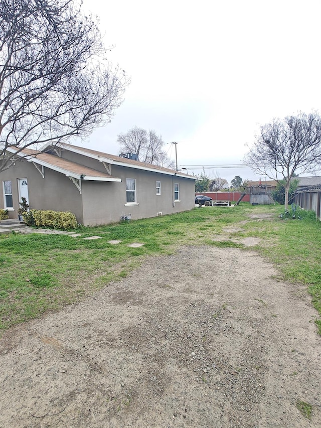 view of side of property with a yard, fence, and stucco siding