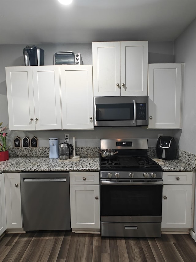 kitchen featuring stainless steel appliances, white cabinets, dark wood-type flooring, and light stone counters