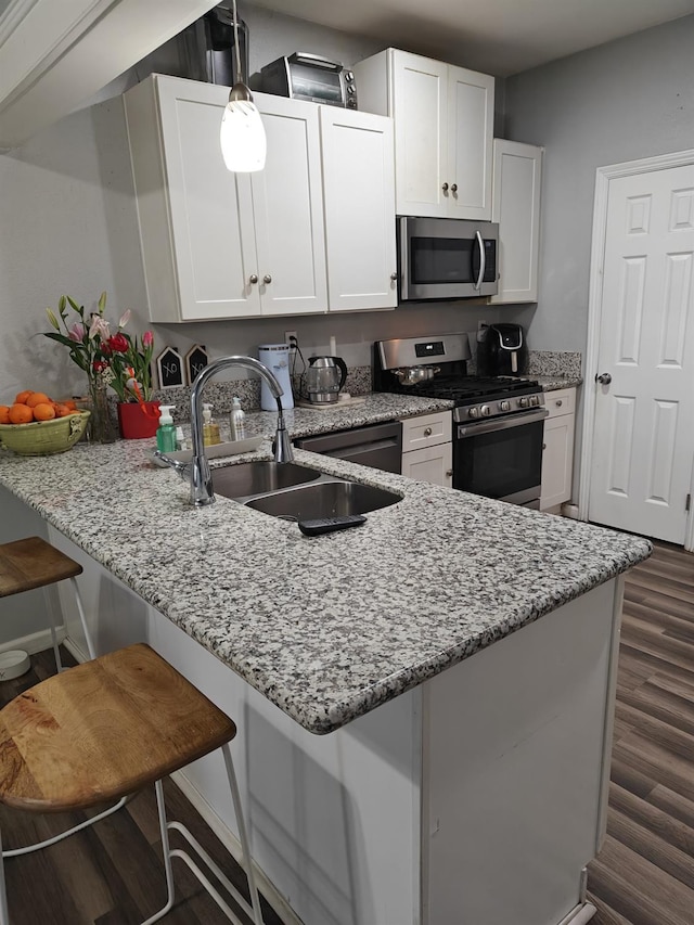 kitchen featuring white cabinets, a breakfast bar area, appliances with stainless steel finishes, a peninsula, and a sink