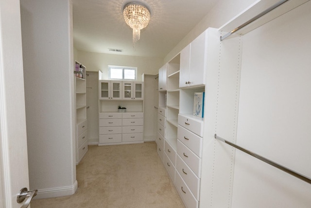 walk in closet with light colored carpet and a chandelier