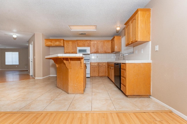 kitchen featuring a breakfast bar area, tile countertops, light tile patterned floors, white appliances, and decorative backsplash