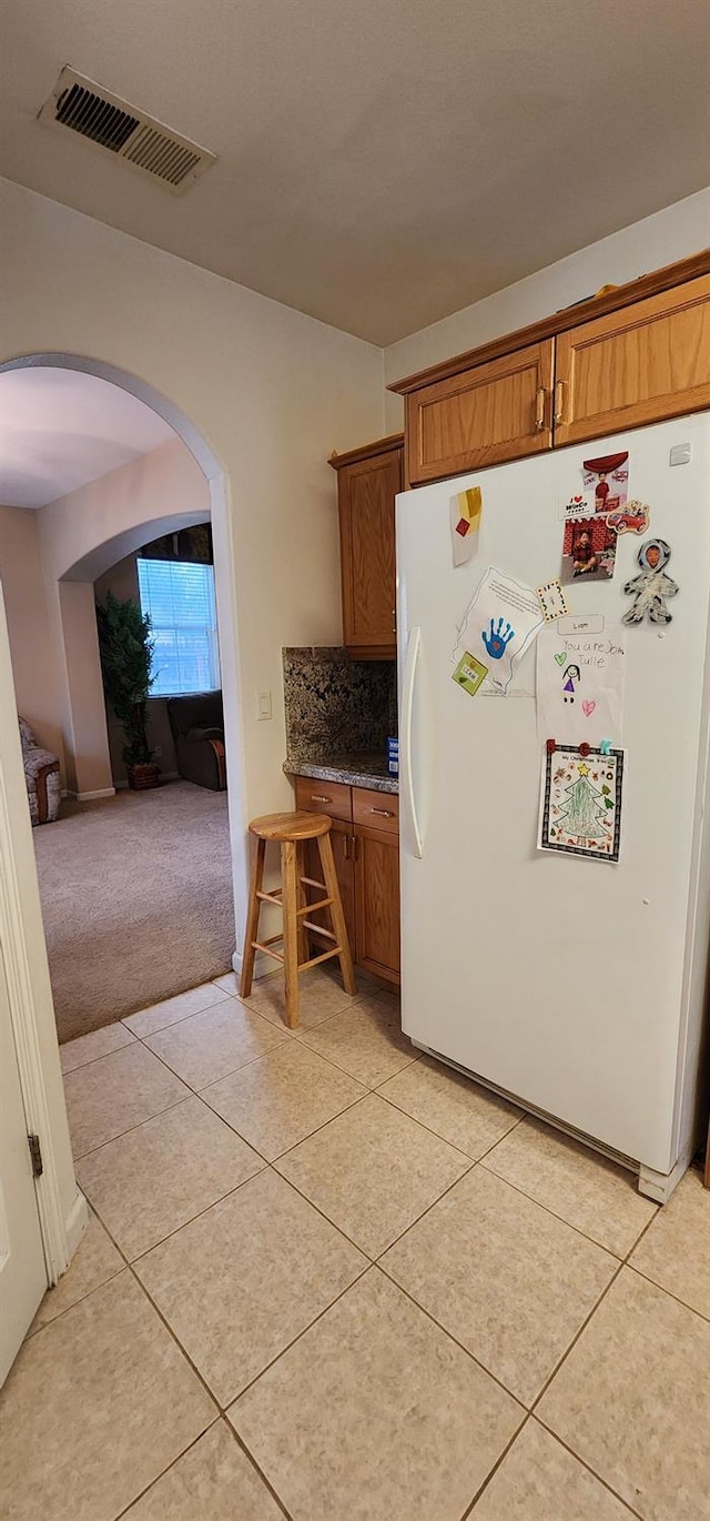 kitchen featuring white fridge, light tile patterned floors, and backsplash