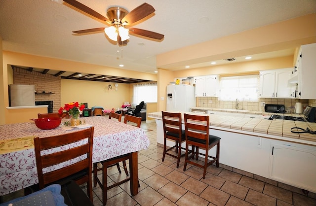 kitchen with backsplash, white refrigerator with ice dispenser, a fireplace, tile counters, and white cabinets