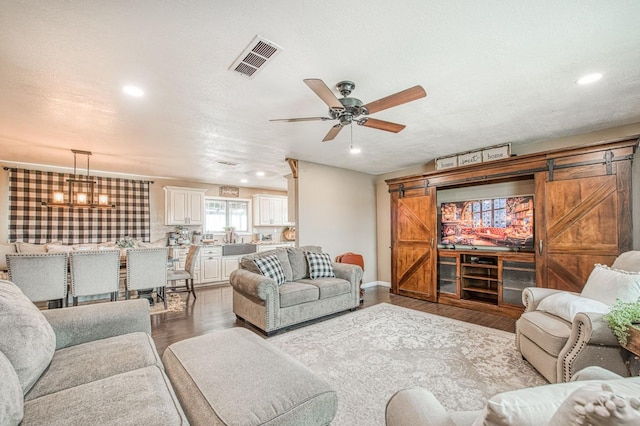 living room featuring wood-type flooring, a barn door, ceiling fan with notable chandelier, and a textured ceiling