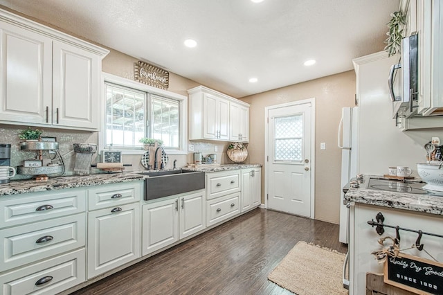 kitchen featuring sink, light stone counters, white refrigerator, dark hardwood / wood-style floors, and white cabinets