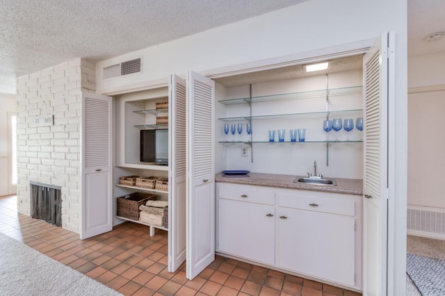 bar with visible vents, a sink, a fireplace, a textured ceiling, and indoor wet bar
