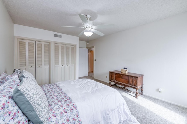 carpeted bedroom with multiple closets, visible vents, a ceiling fan, baseboards, and a textured ceiling