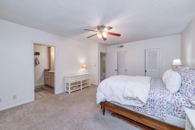 bedroom featuring light carpet, a textured ceiling, ensuite bathroom, visible vents, and a ceiling fan