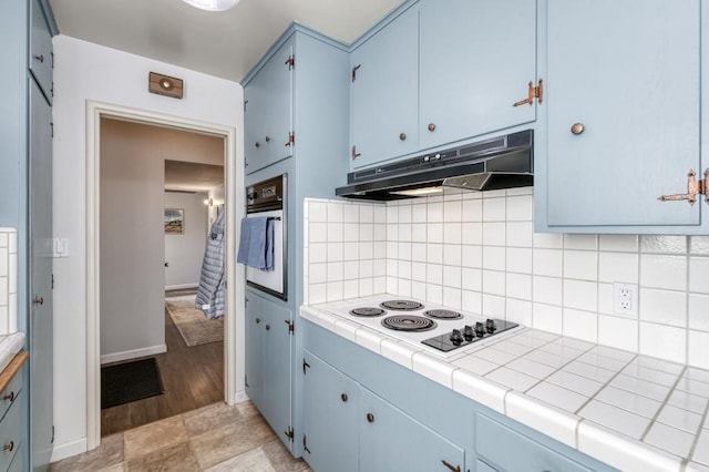 kitchen with white appliances, blue cabinetry, tile countertops, and decorative backsplash