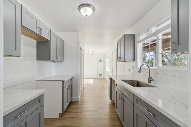 kitchen featuring gray cabinets, light hardwood / wood-style flooring, sink, and backsplash