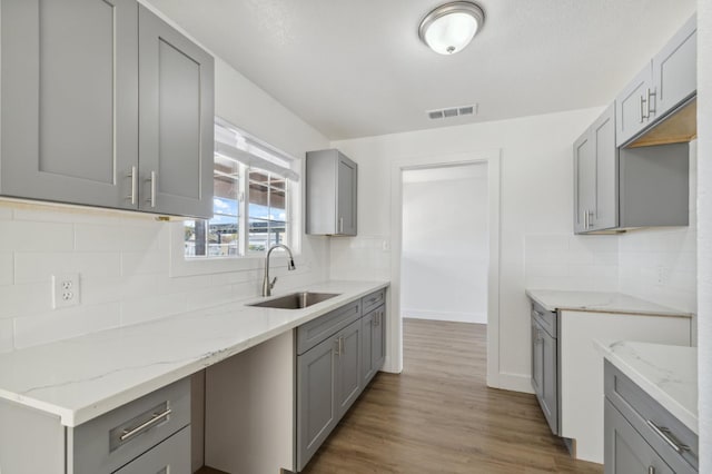 kitchen with light hardwood / wood-style flooring, sink, backsplash, light stone counters, and gray cabinetry