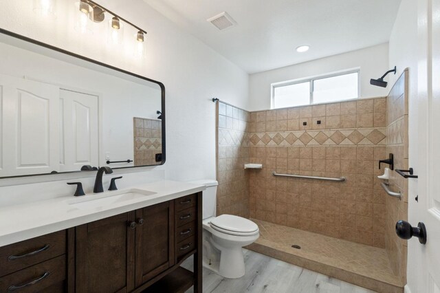 bathroom with wood-type flooring, toilet, a tile shower, and vanity