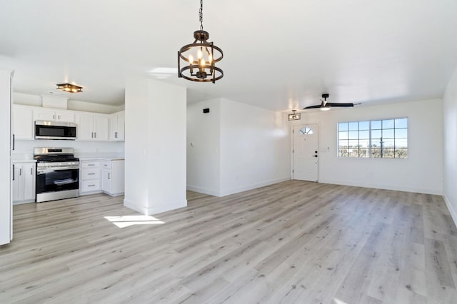 interior space with appliances with stainless steel finishes, white cabinets, pendant lighting, ceiling fan with notable chandelier, and light wood-type flooring