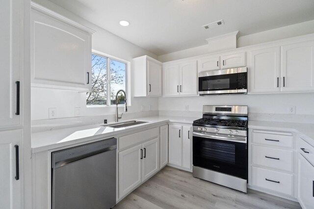 kitchen with sink, appliances with stainless steel finishes, white cabinetry, and light wood-type flooring