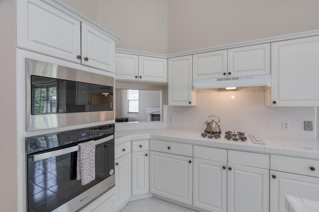 kitchen with decorative backsplash, white cabinetry, tile countertops, and stainless steel microwave