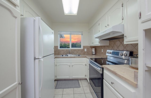 kitchen featuring sink, light tile patterned flooring, stainless steel range with electric stovetop, white cabinetry, and white refrigerator