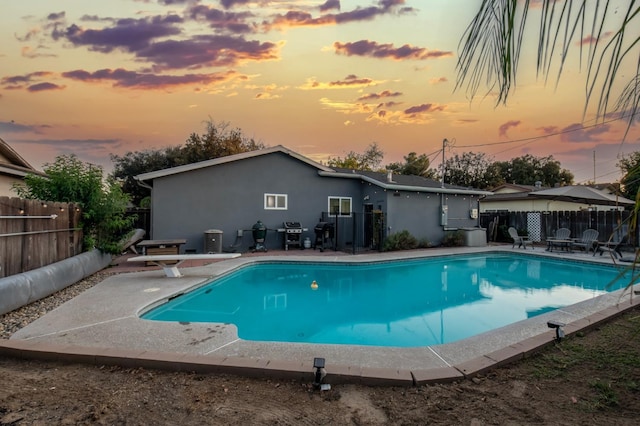 pool at dusk featuring a diving board, grilling area, and a patio