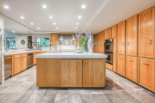 kitchen with a tray ceiling, a center island with sink, appliances with stainless steel finishes, and wall chimney exhaust hood