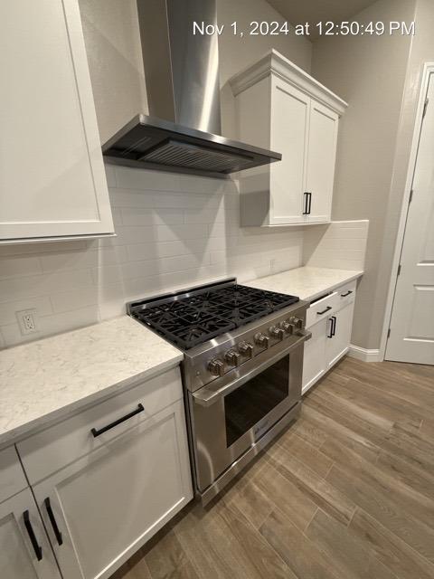 kitchen with stainless steel stove, white cabinets, wall chimney range hood, decorative backsplash, and dark hardwood / wood-style floors