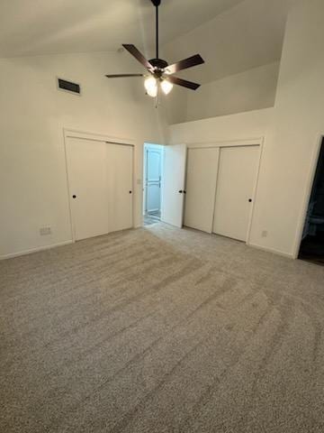 unfurnished bedroom featuring high vaulted ceiling, carpet flooring, and two closets