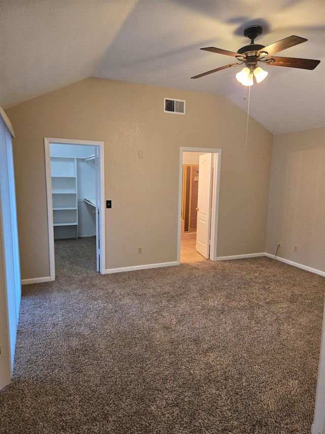 unfurnished bedroom featuring ceiling fan, carpet flooring, vaulted ceiling, and a walk in closet