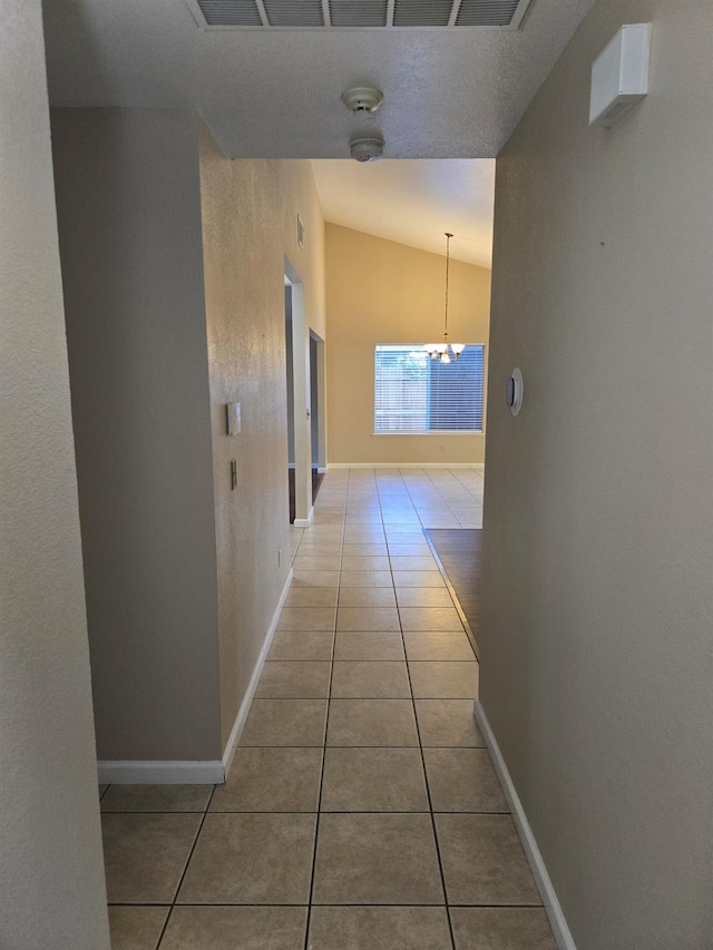 hallway featuring vaulted ceiling, an inviting chandelier, and light tile patterned floors