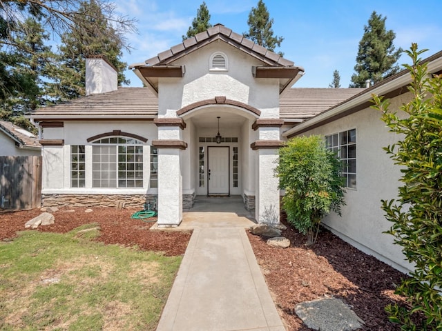 view of front of property with fence, a tiled roof, stucco siding, a chimney, and stone siding