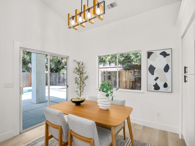 dining space featuring light wood-type flooring, high vaulted ceiling, and a notable chandelier