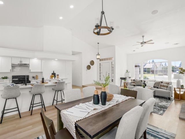 dining area featuring ceiling fan with notable chandelier, high vaulted ceiling, and light wood-type flooring