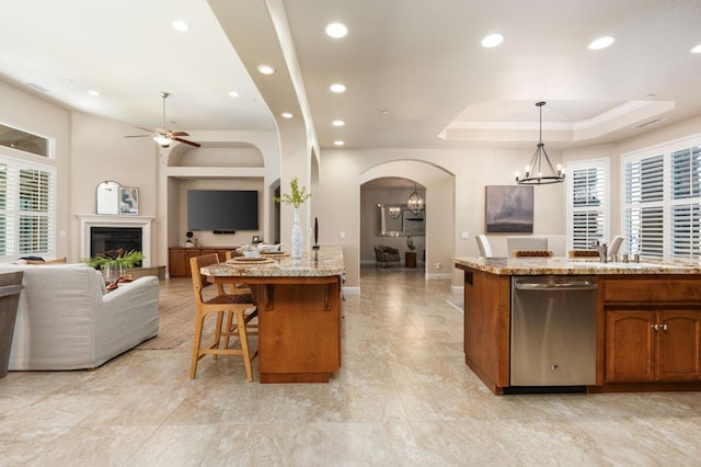 kitchen featuring a tray ceiling, stainless steel dishwasher, a kitchen island with sink, and hanging light fixtures