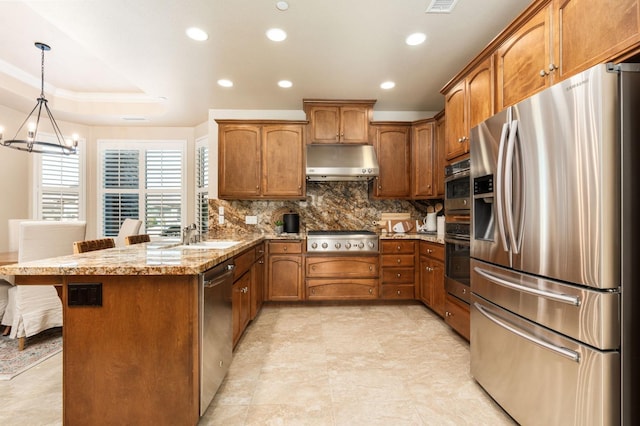 kitchen with appliances with stainless steel finishes, light stone counters, pendant lighting, backsplash, and a kitchen bar