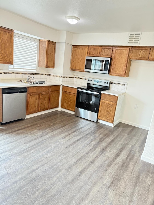 kitchen with stainless steel appliances, light wood-type flooring, brown cabinetry, and visible vents