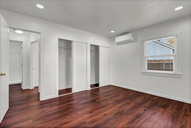 unfurnished bedroom with two closets, dark wood-type flooring, and a wall mounted AC